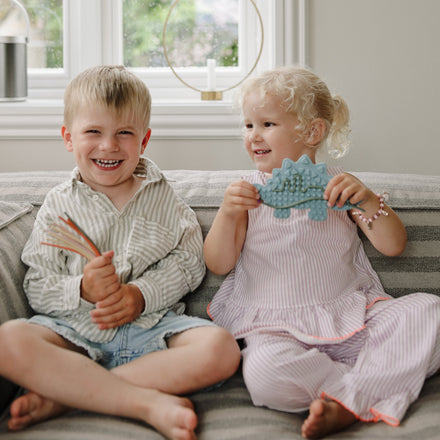 Kinderen spelen met het Mushie sensorisch speelgoed Dino in de zetel