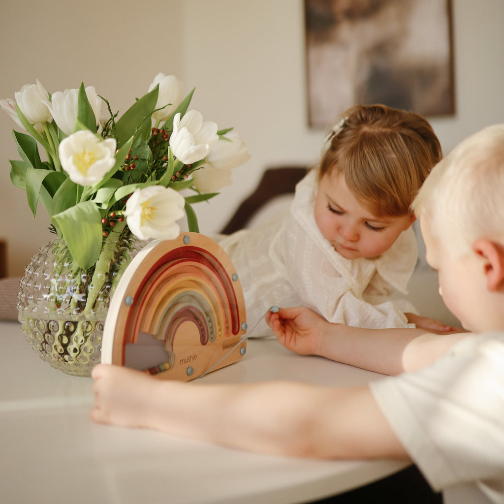 Twee kinderen spelen samen met het Mushie magnetisch doolhof Regenboog aan tafel