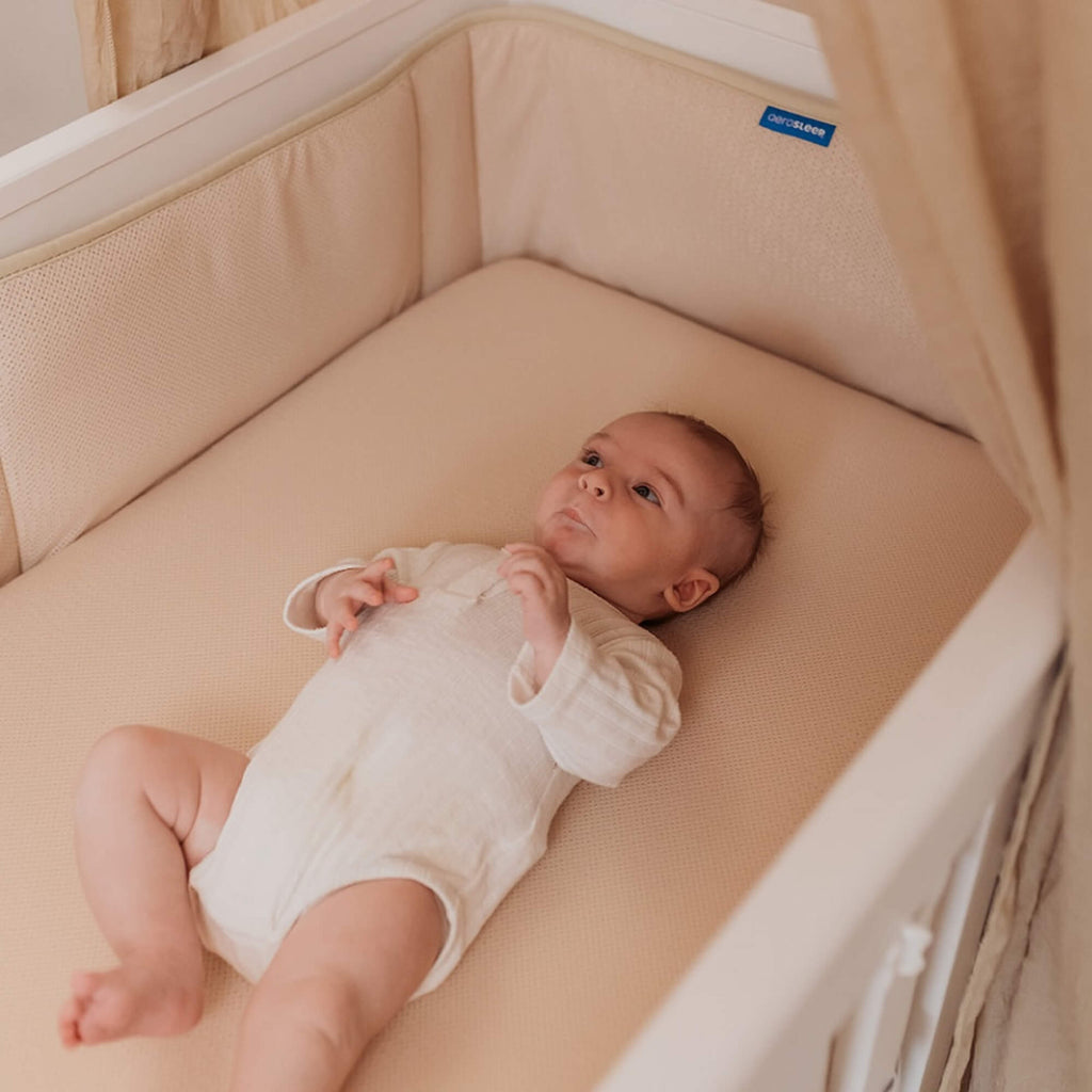 Baby in een babybed met Aerosleep bedomrander almond