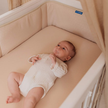 Baby in een babybed met Aerosleep bedomrander almond