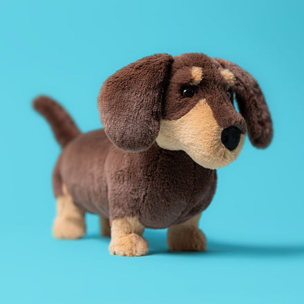 Jellycat Otto Sausage Dog knuffelhond op een blauwe achtergrond