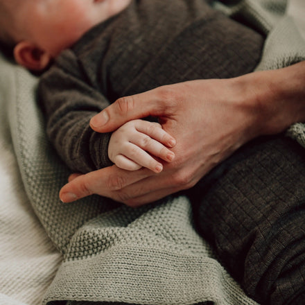 Koeka Wiegdeken Lisbon in olive, baby met de deken in de armen van een ouder
